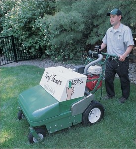 Male Lawn Doctor employee wheeling a lawn seeding machine over the lawn