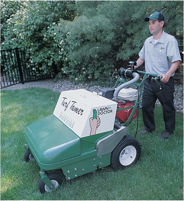 Male Lawn Doctor employee wheeling a turf tamer machine performing lawn seeding services