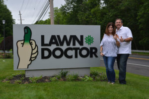 Lawn Doctor of Jax Beaches owners standing beside lawn care lawn doctor sign