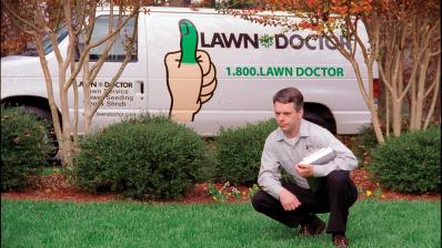 lawn doctor lawn care technician inspecting a lawn in front of van