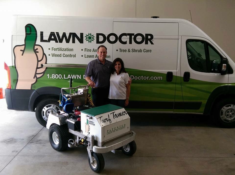 two people standing by of lawn doctor truck and turf tamer