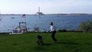 A man seeding a lawn next to a lake for lawn services in Waltham