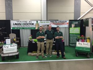 three men in front of lawn doctor booth