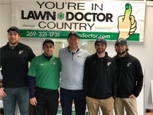 five employees in front of lawn doctor banner