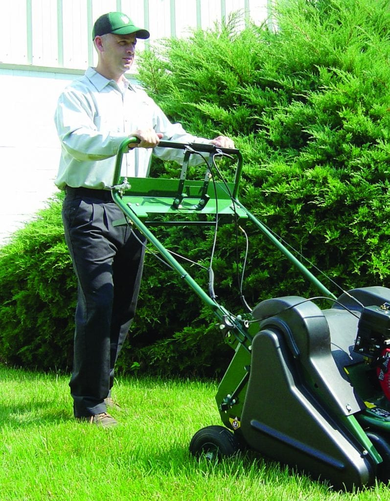 lawn care technician pushing aerator over a green lawn